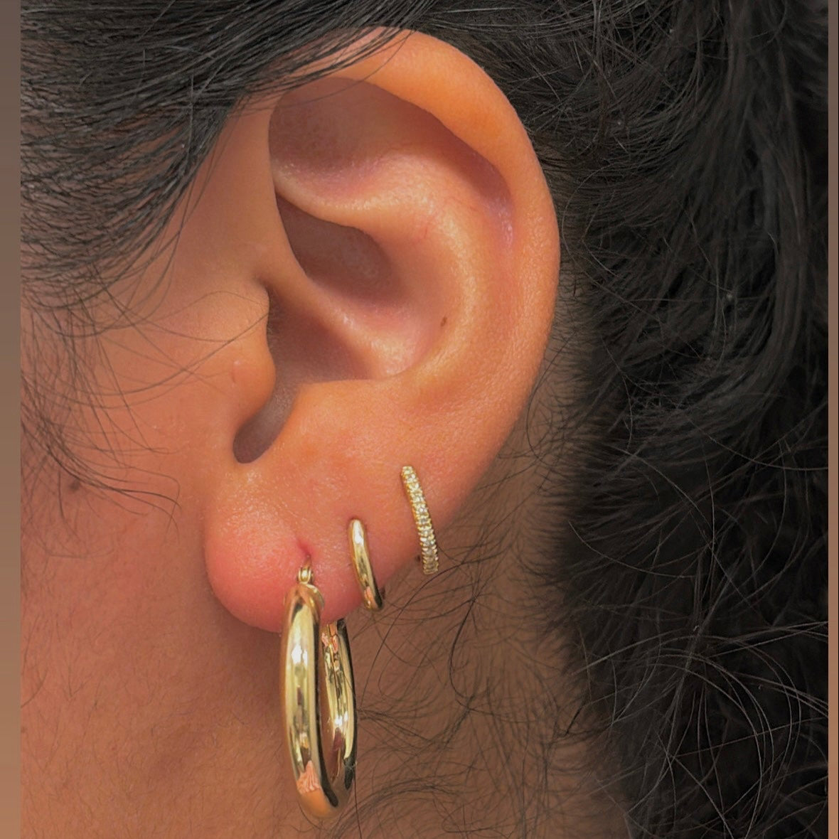 Close-up of an ear wearing gold hoop earrings with a blurred background