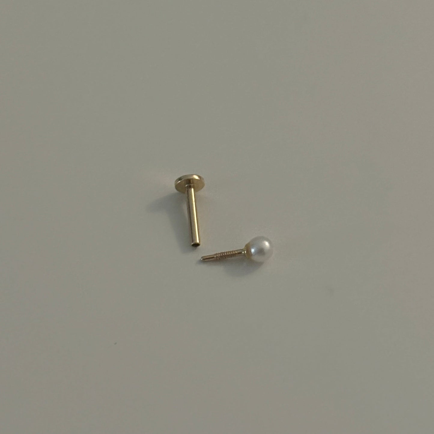 Gold earring with pearl on a light gray background