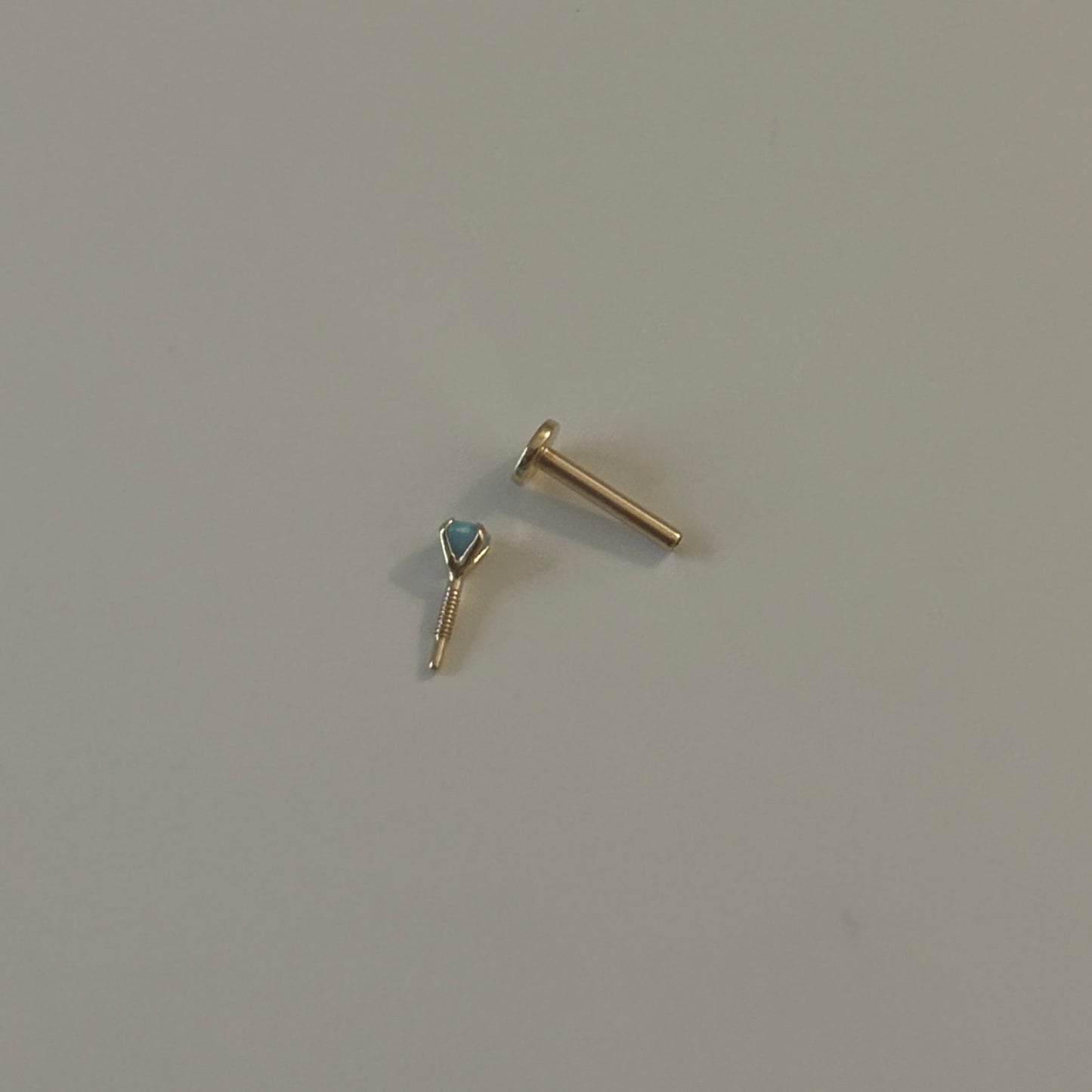 Gold earring with a blue gemstone on a light gray background