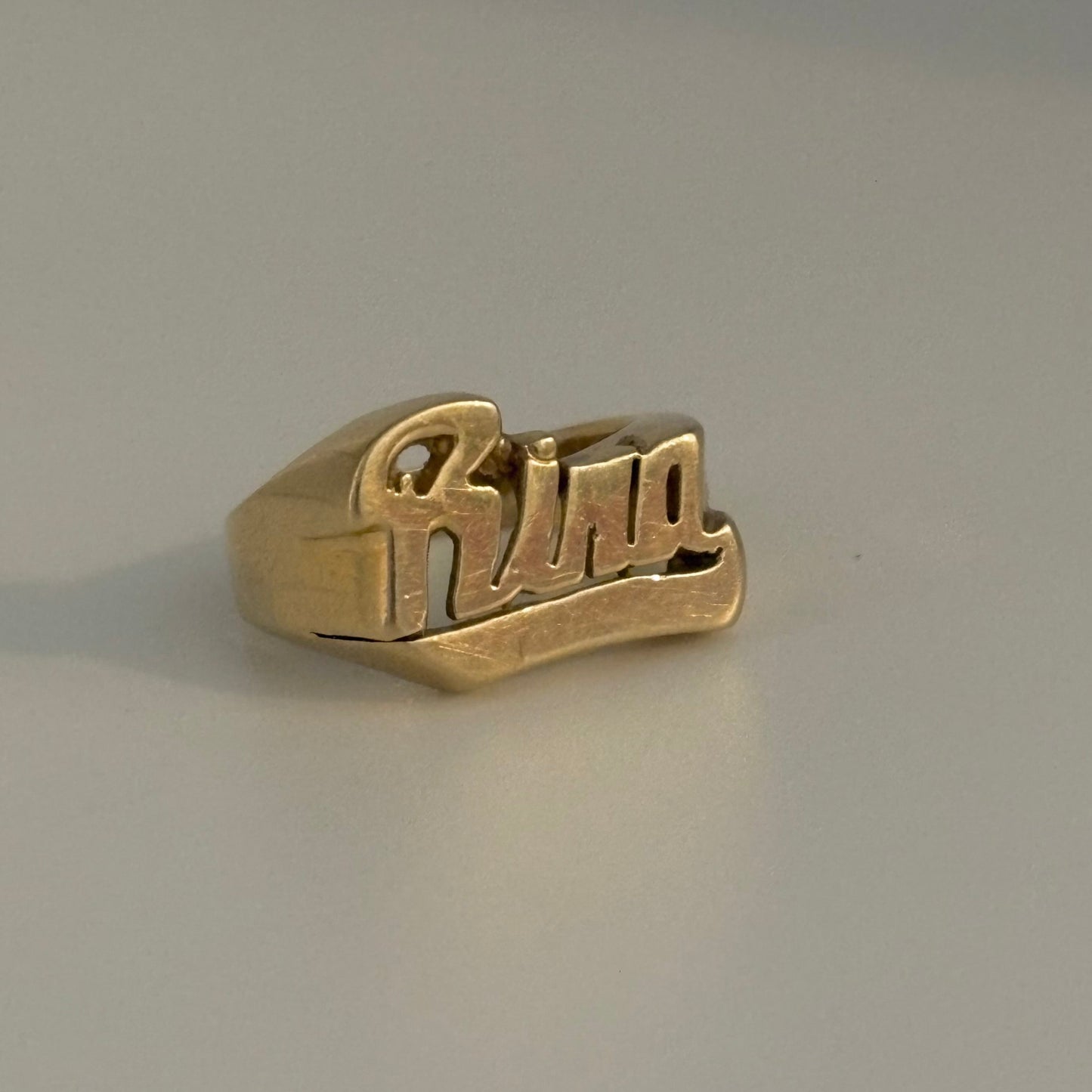 Gold ring with 'Rina' engraving on a gray background