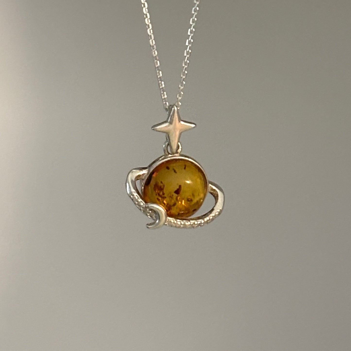 Necklace with a pendant featuring an amber stone and star design on a gray background