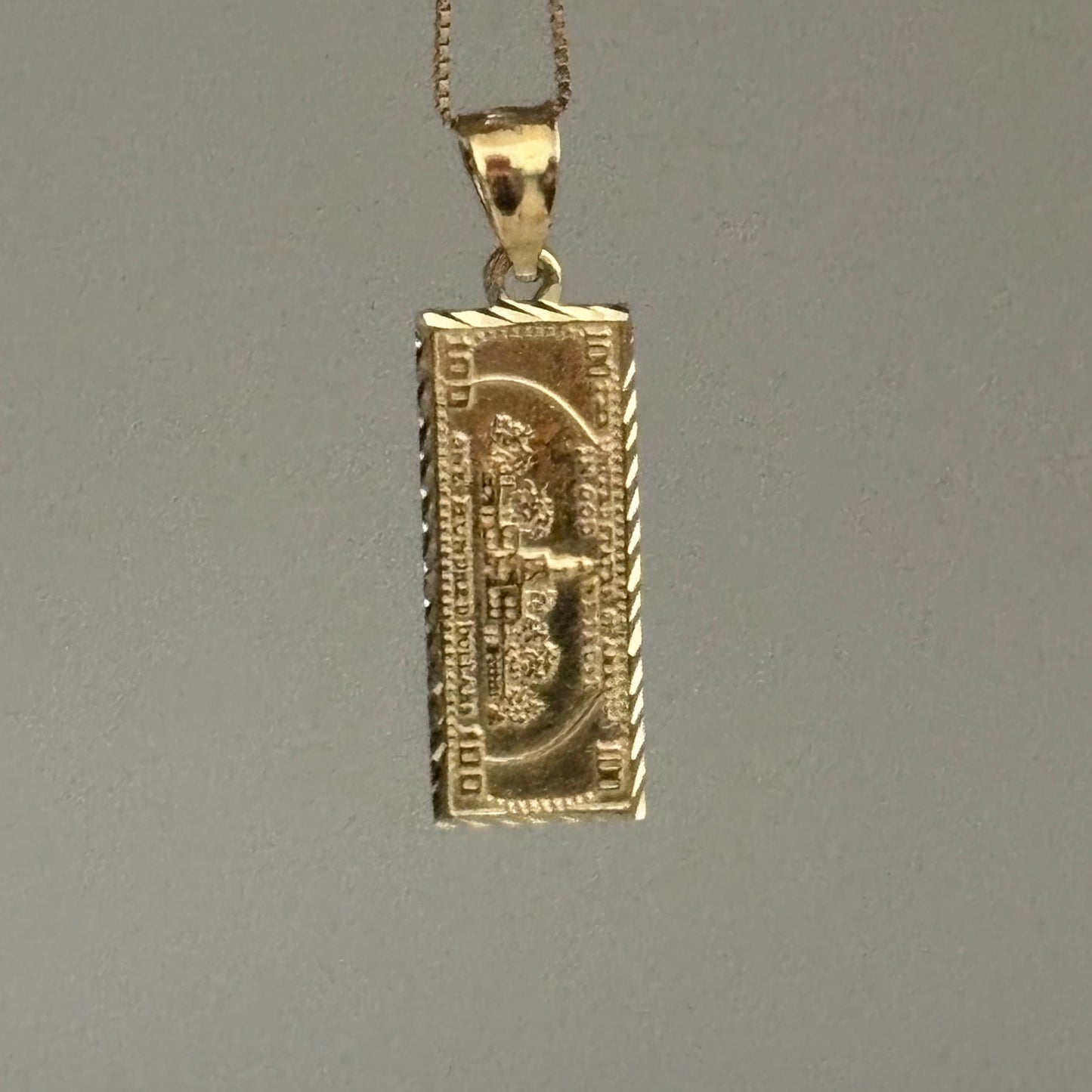 Gold dollar bill pendant on a gray background