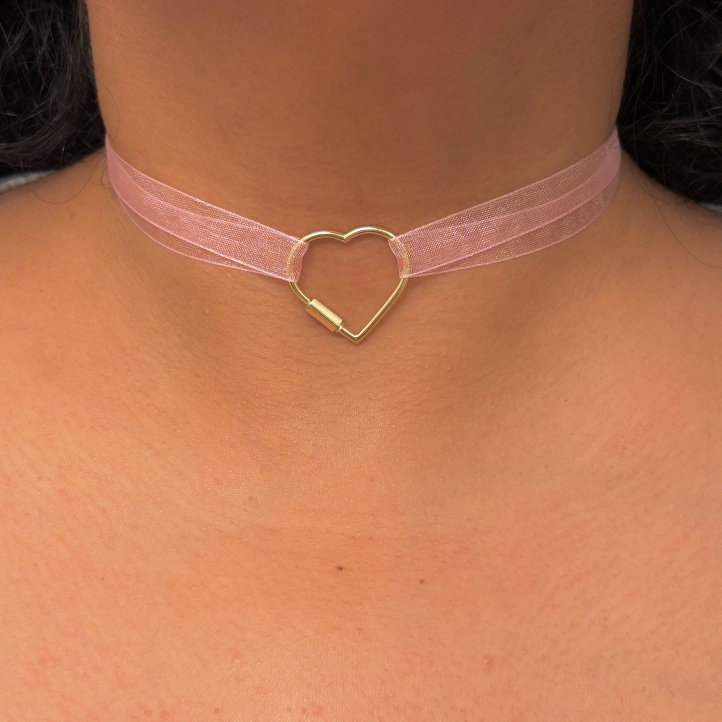 Pink choker with a gold heart-shaped clasp on a person's neck.