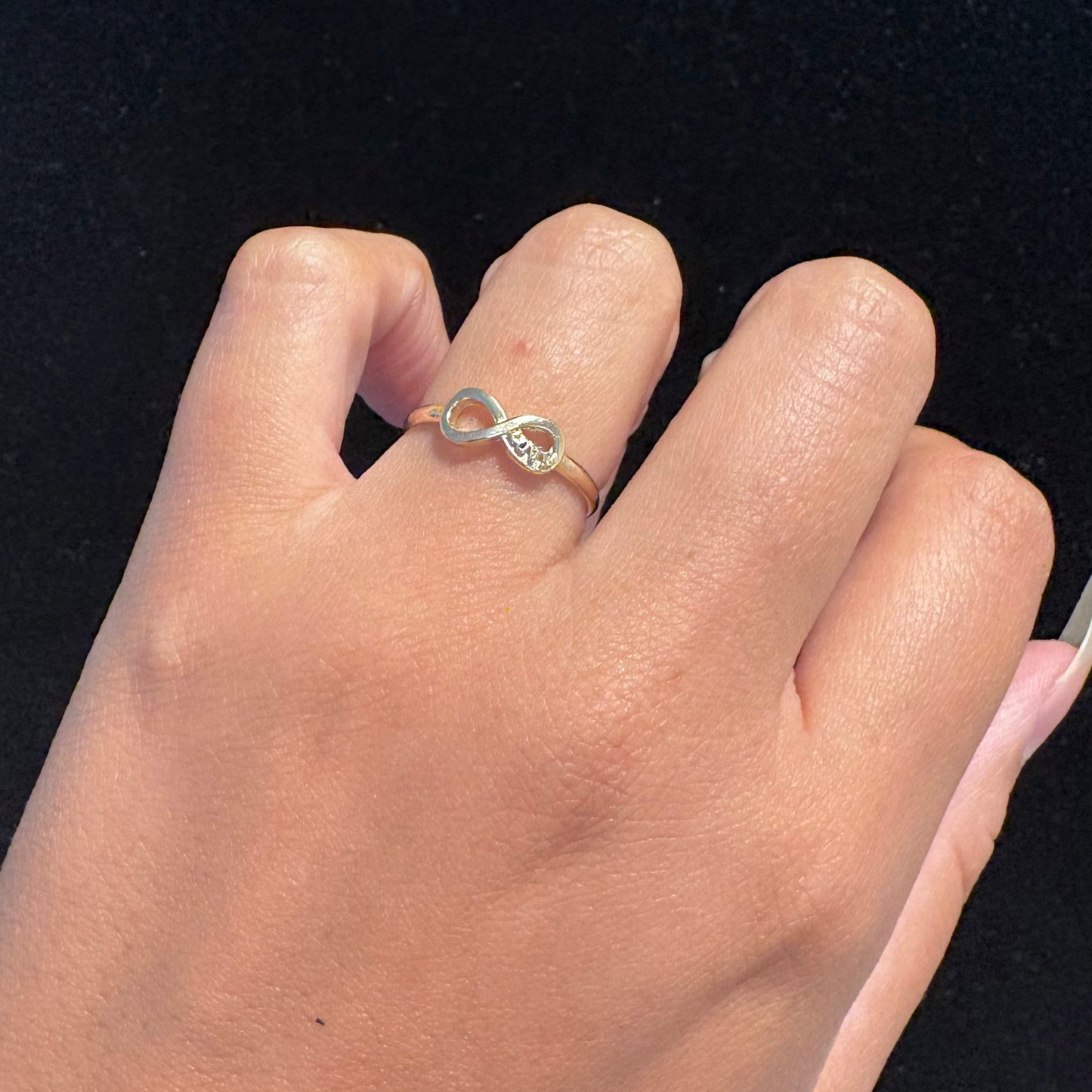 Hand wearing a silver infinity ring on a black background