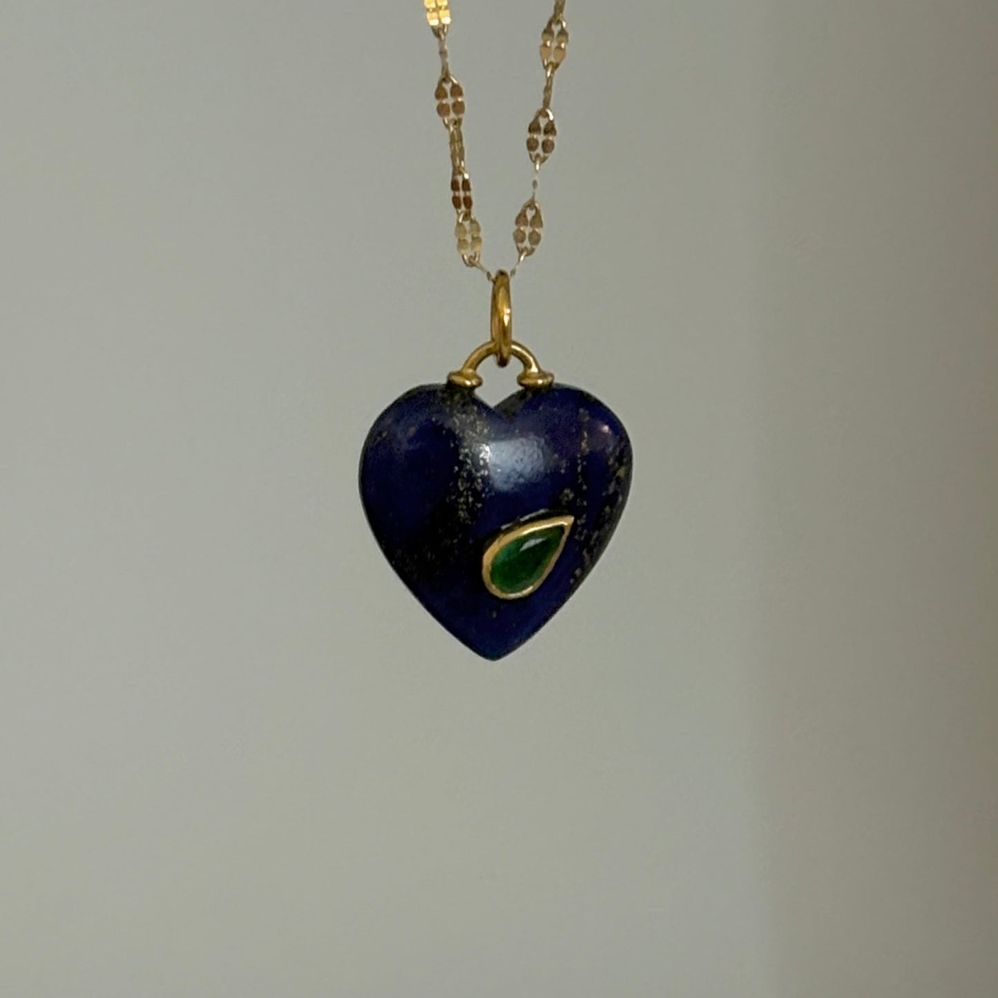 Heart-shaped pendant necklace with blue stone and gold chain on a gray background