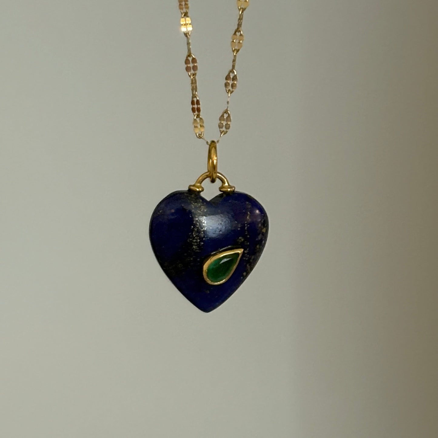 Navy heart-shaped pendant with gold chain on a gray background