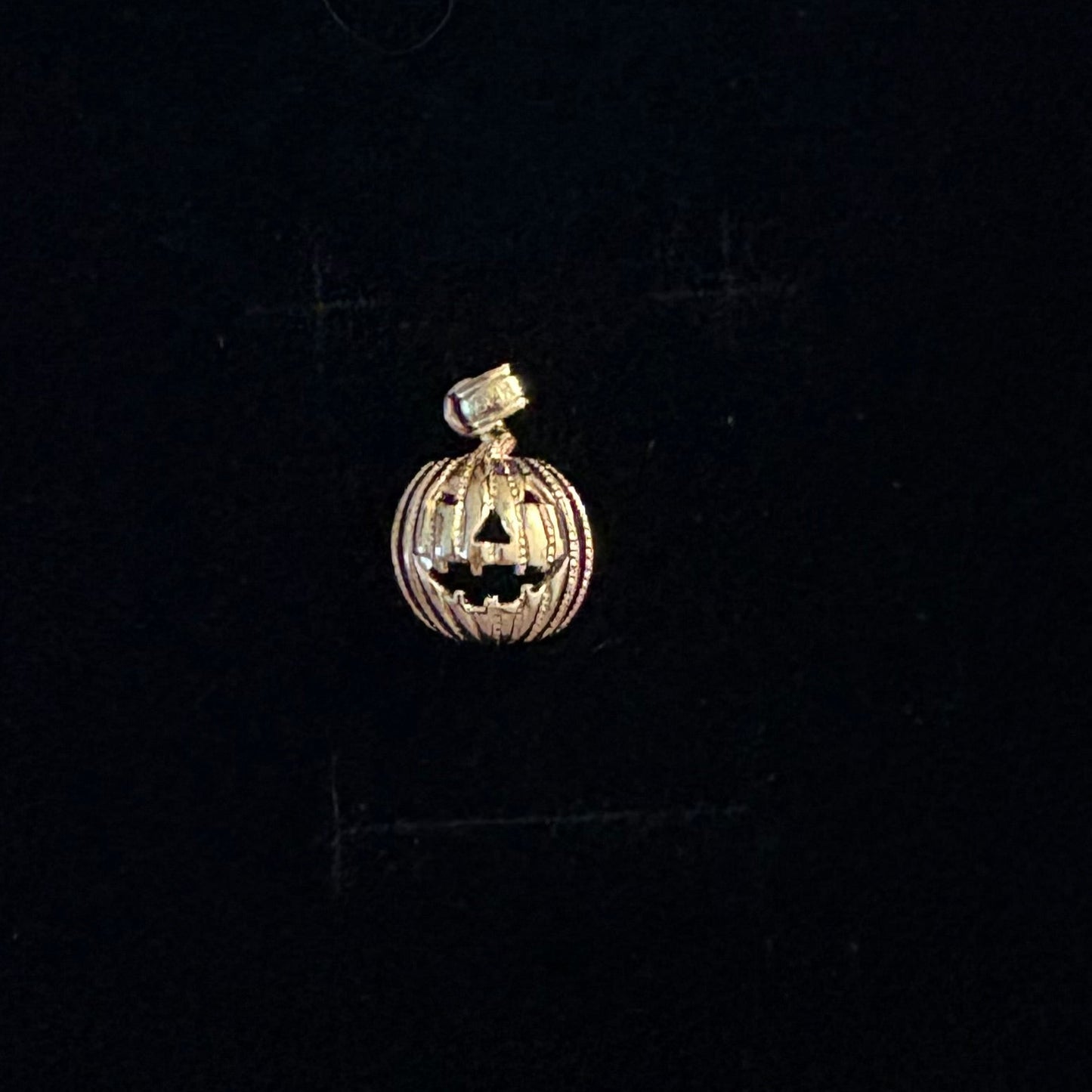 14K gold pumpkin charm with jack-o’-lantern face, Halloween pendant on black background