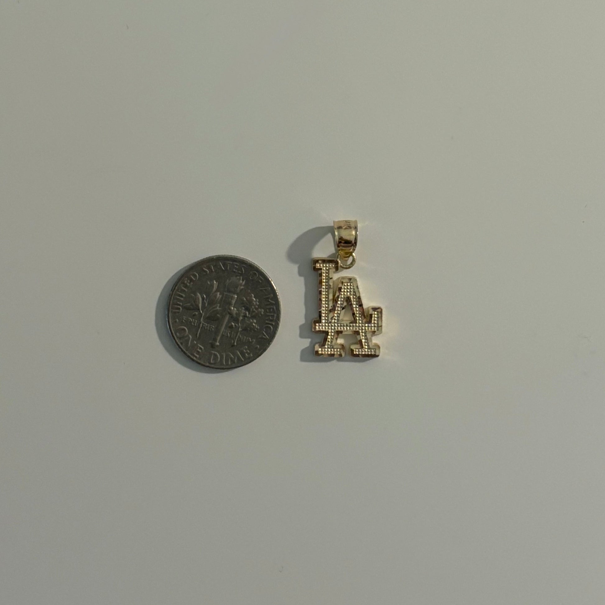Small gold pendant with 'LA' initials next to a coin on a gray background