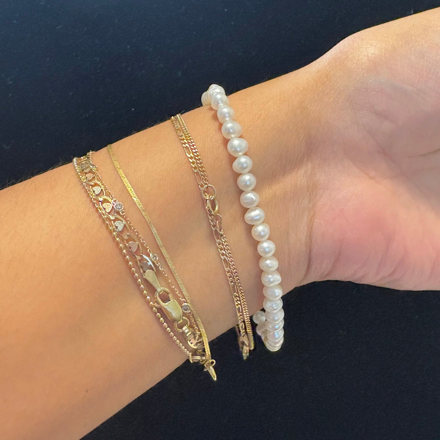 Wrist with multiple gold and pearl bracelets on a dark background