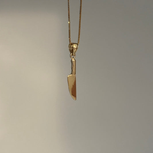 Gold knife-shaped pendant on a chain against a gray background