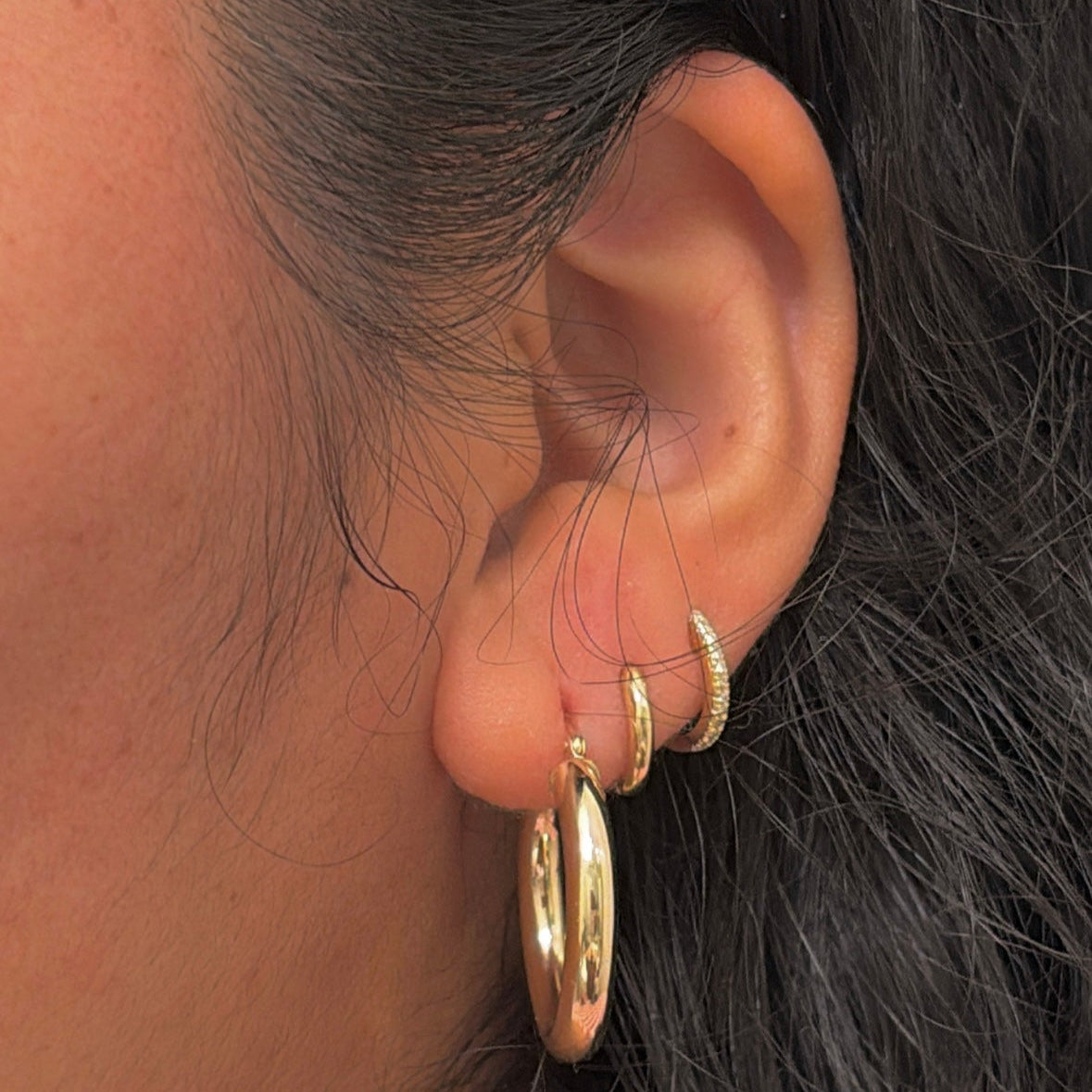 Close-up of an ear wearing gold hoop earrings with dark hair.