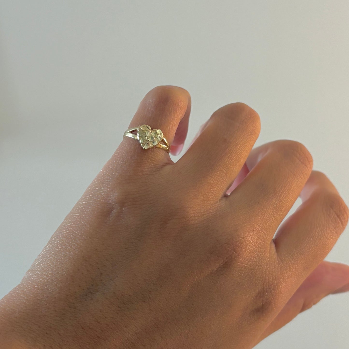 Hand wearing a gold ring with a diamond on a plain background