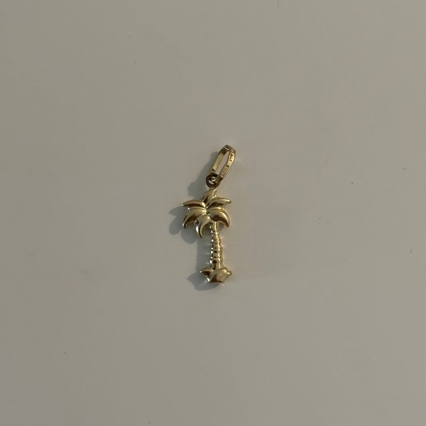 Gold palm tree charm on a light gray background
