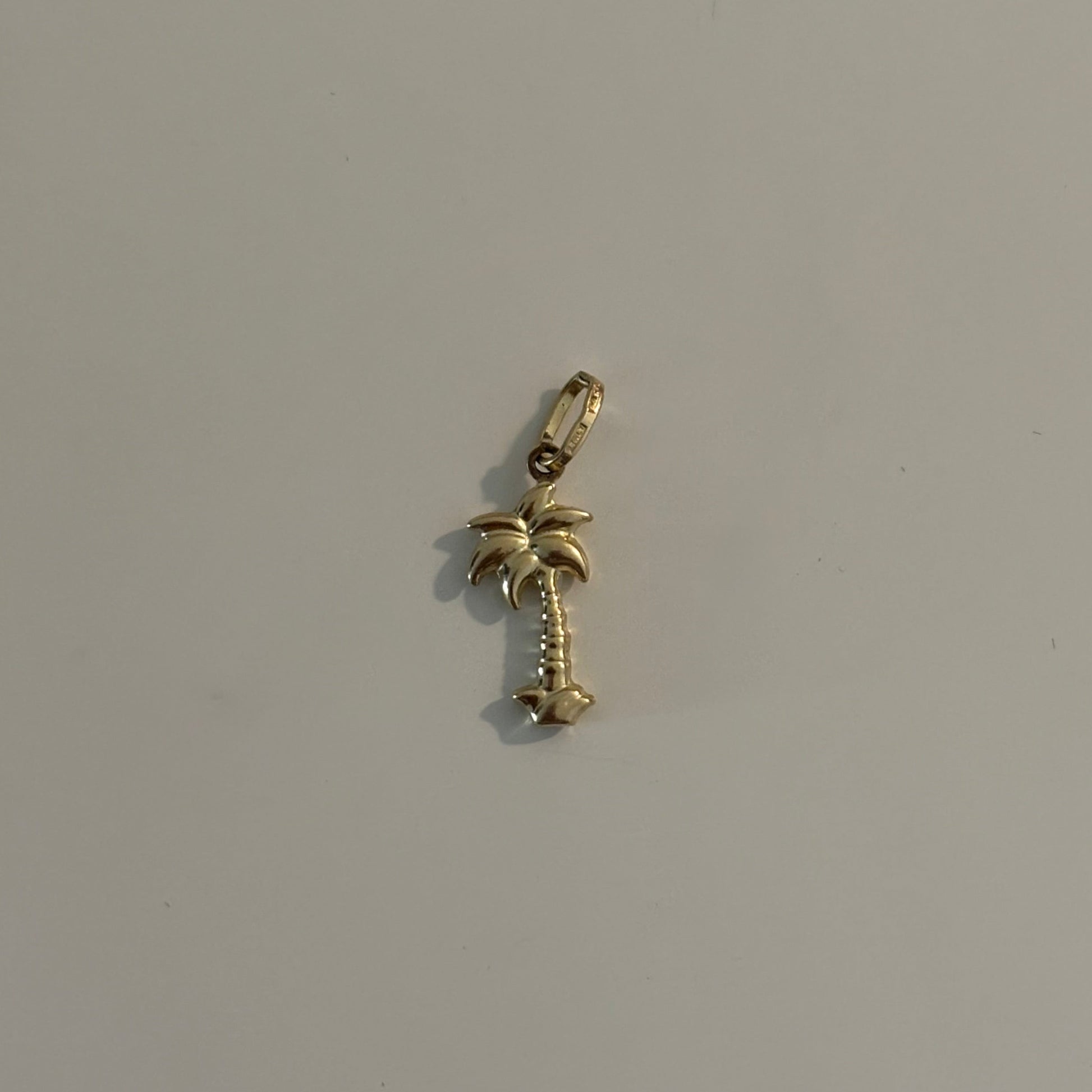 Gold palm tree charm on a light gray background