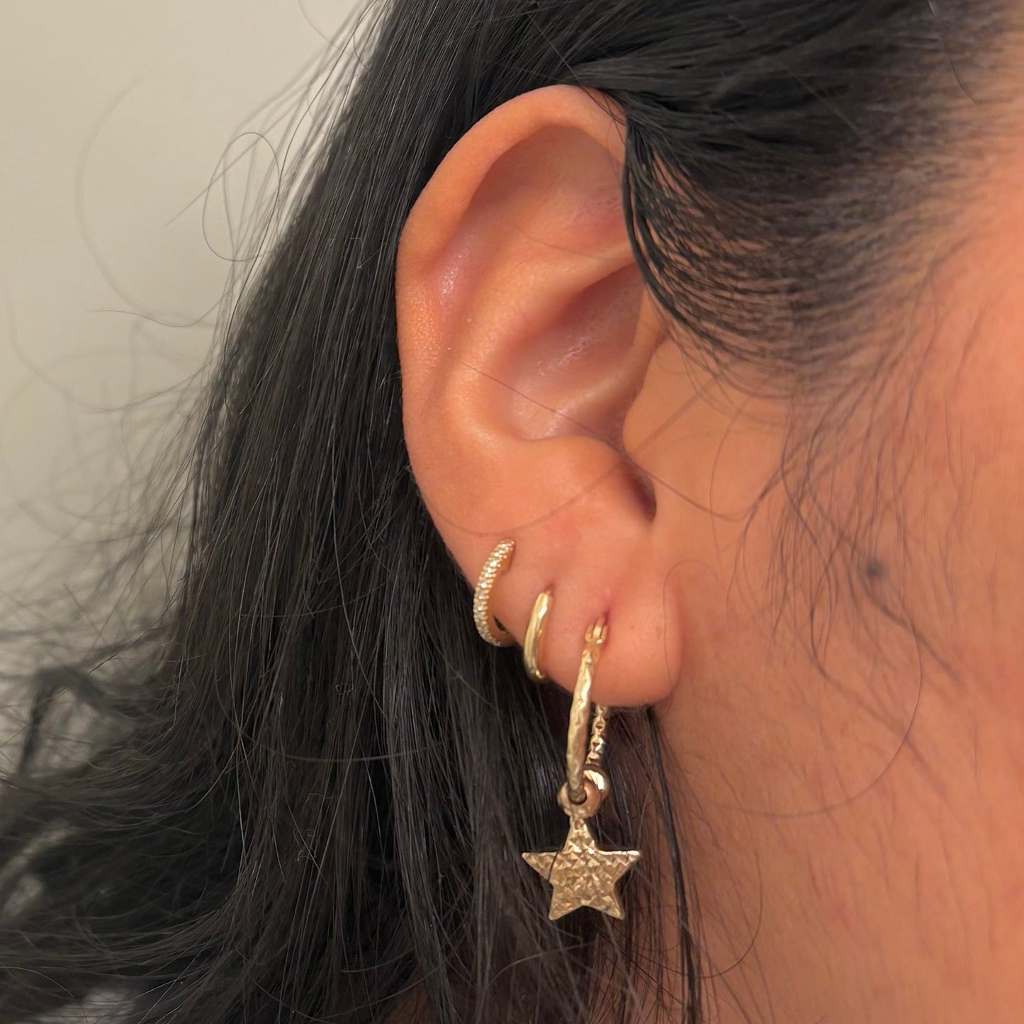 Close-up of an ear wearing a gold star-shaped earring with a neutral background