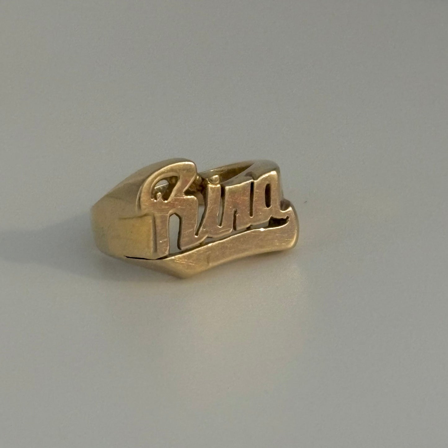 Gold ring with 'rina' engraving on a gray background