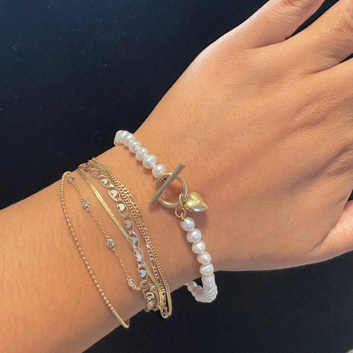 Hand wearing multiple gold and pearl bracelets on a dark background