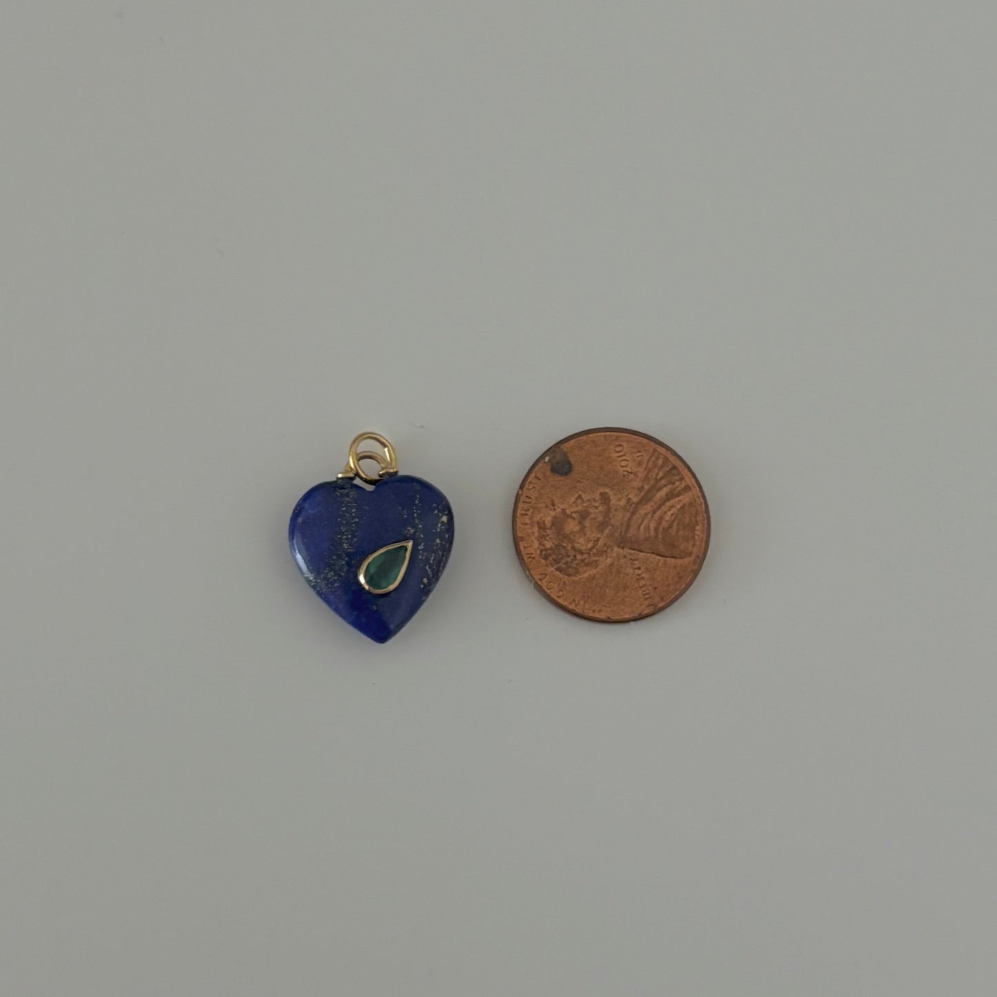 Blue heart-shaped pendant with green stone next to a penny on a white background