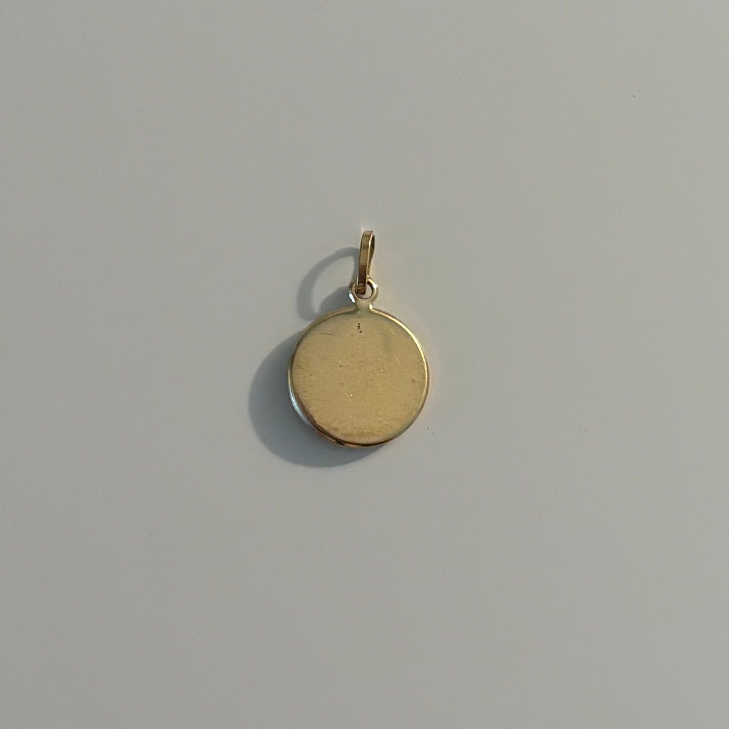 A small round gold pendant charm with a flat, polished surface and a top loop, shown on a plain light gray background.