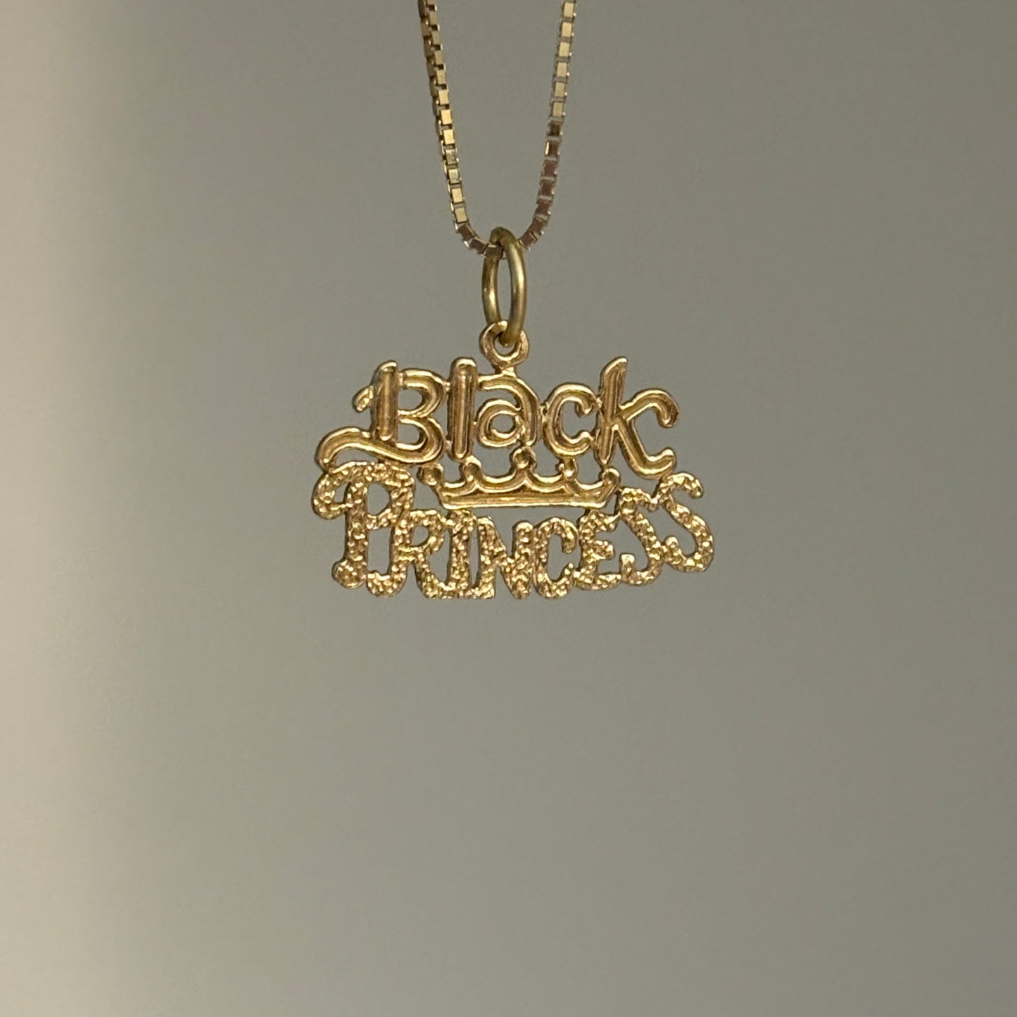 Gold necklace with black princess pendant on a gray background