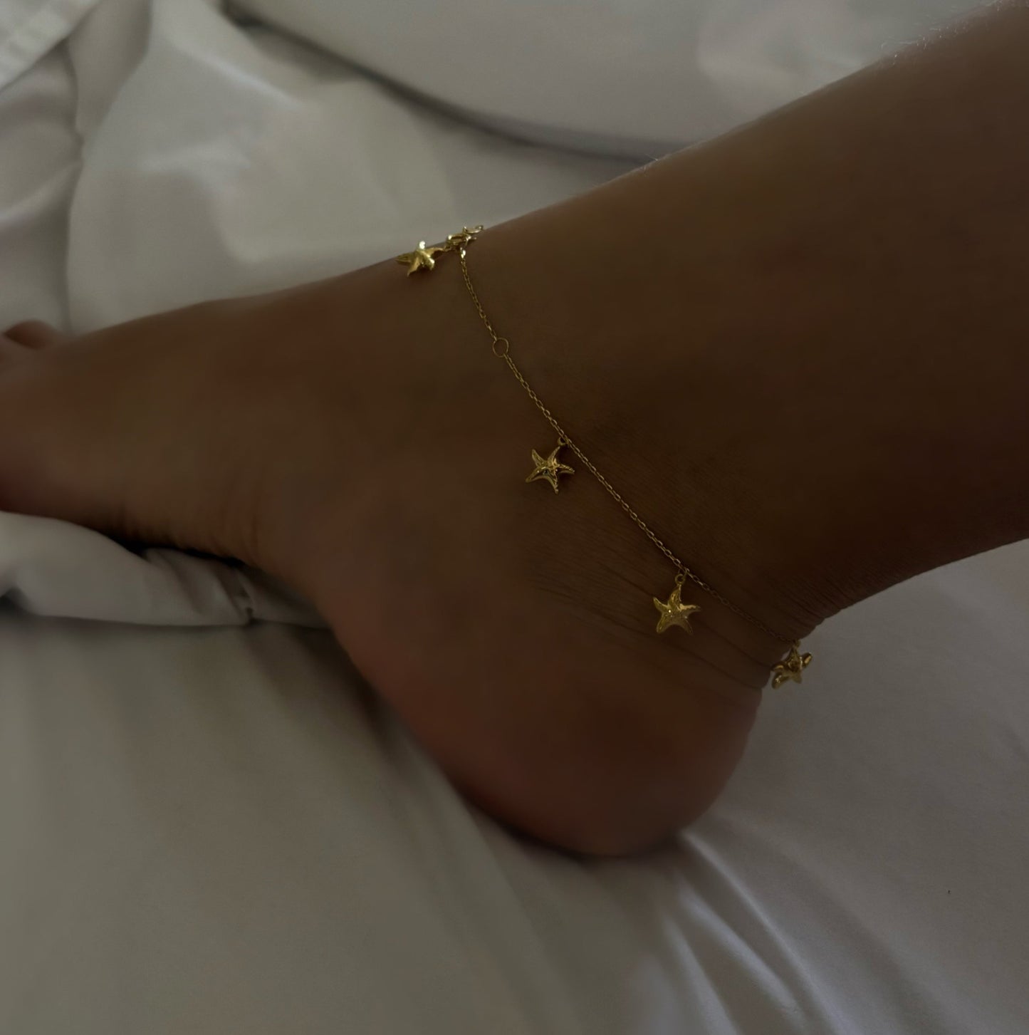 Gold anklet with star charms on a foot against a white background