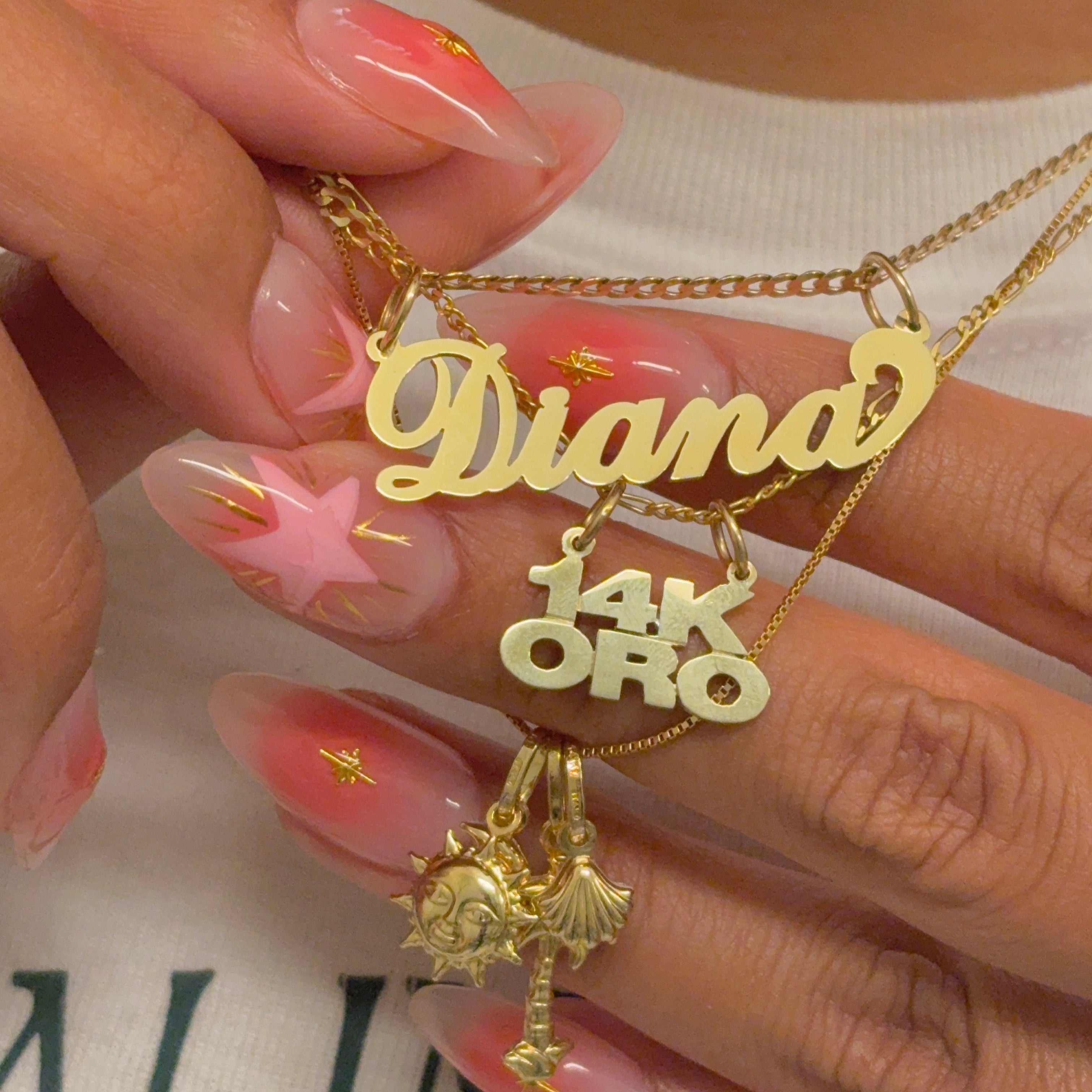 Gold necklaces with name pendants held by a person with pink nail polish.