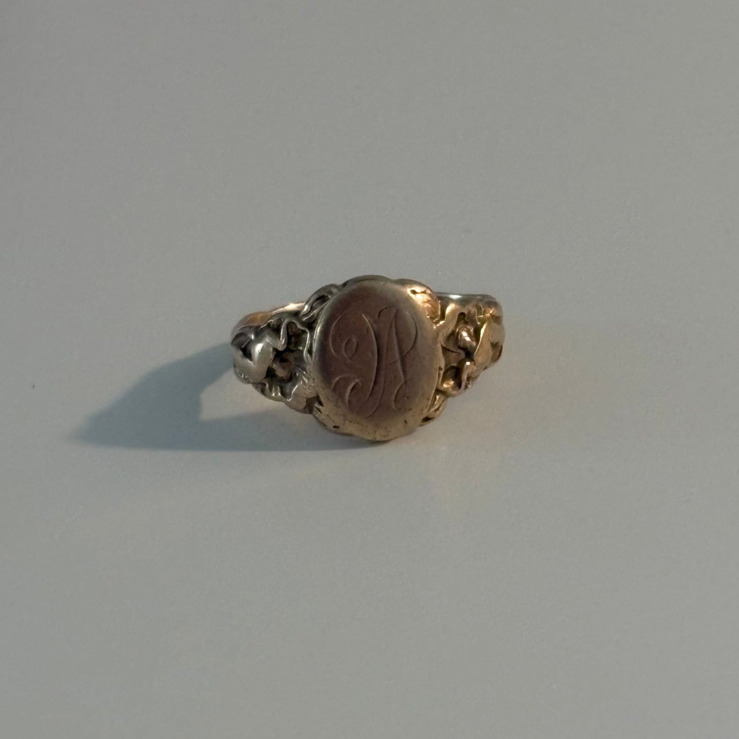 A vintage signet ring with a gold-toned band and a round, polished brown or bronze-colored face, photographed on a plain light gray surface.