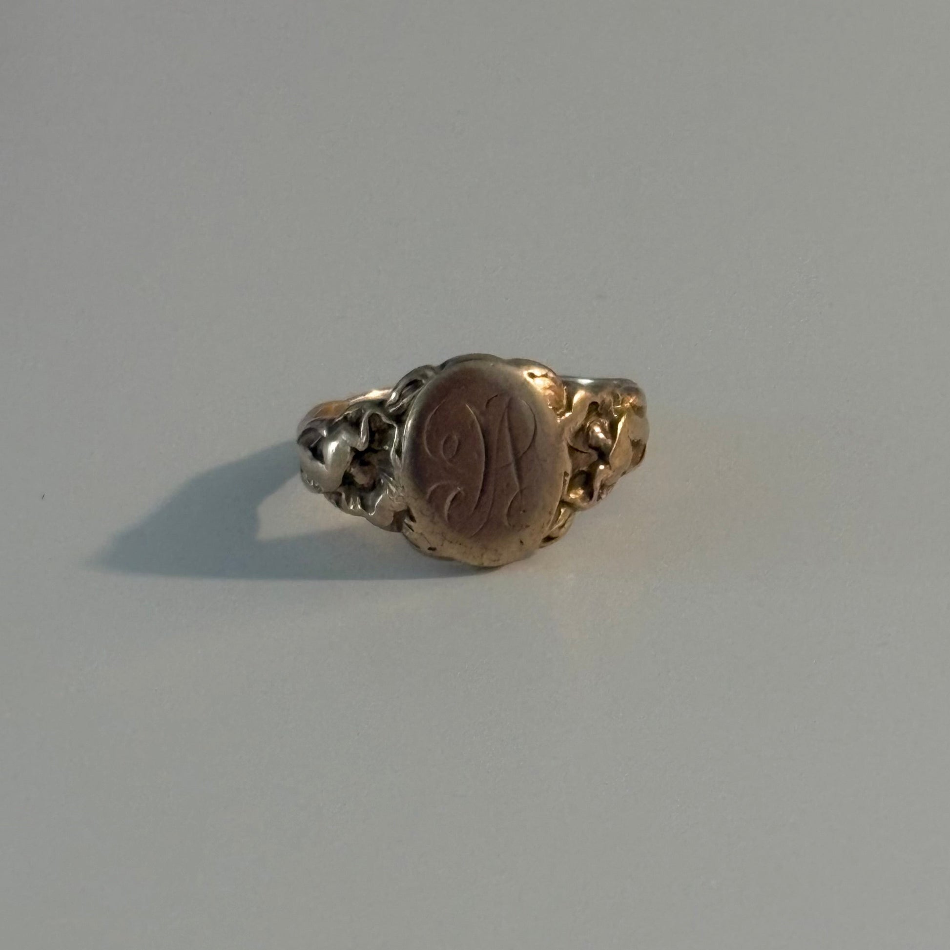 A vintage signet ring with a gold-toned band and a round, polished brown or bronze-colored face, photographed on a plain light gray surface.