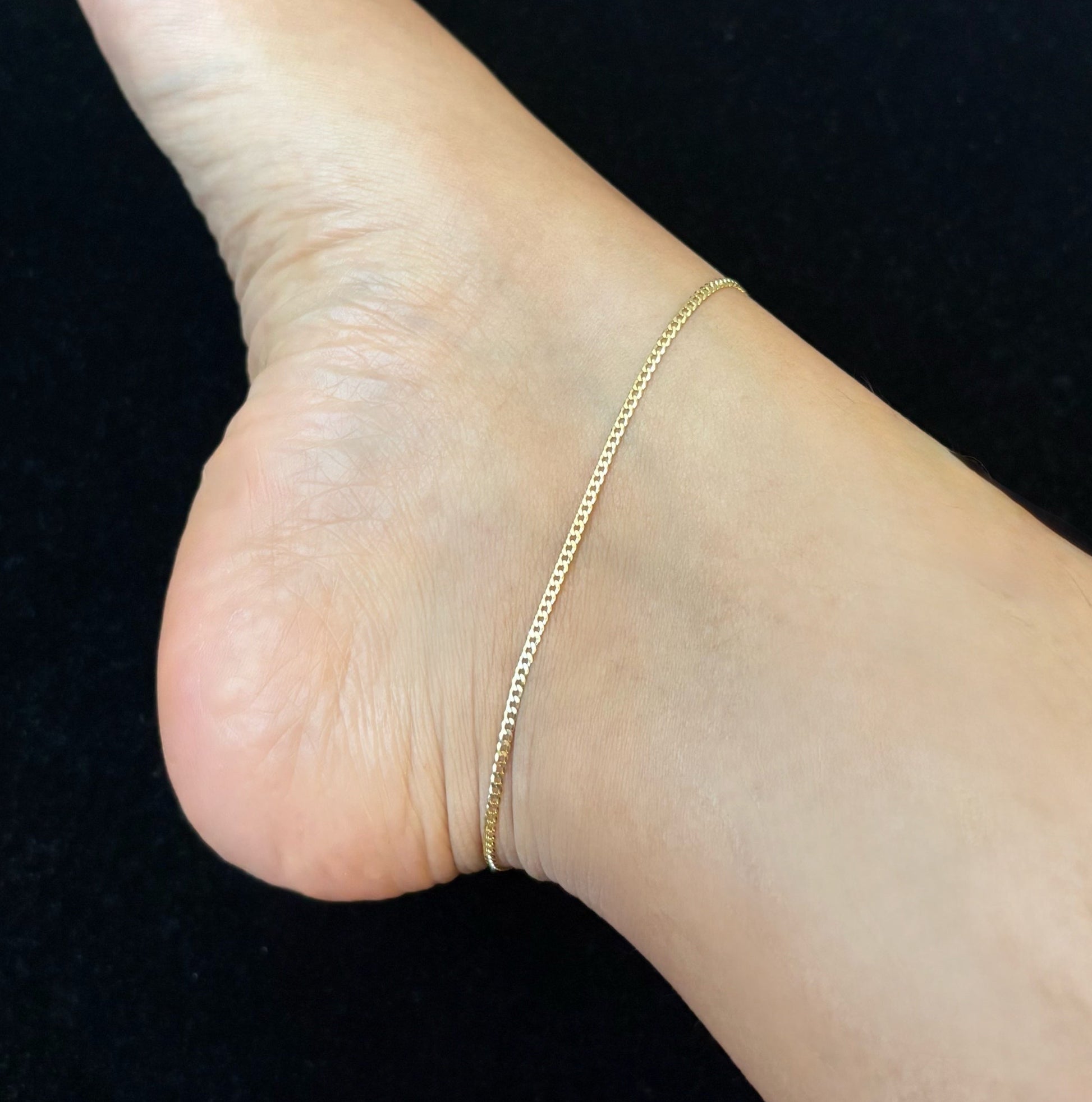 Close-up of a foot wearing a gold anklet on a black surface.