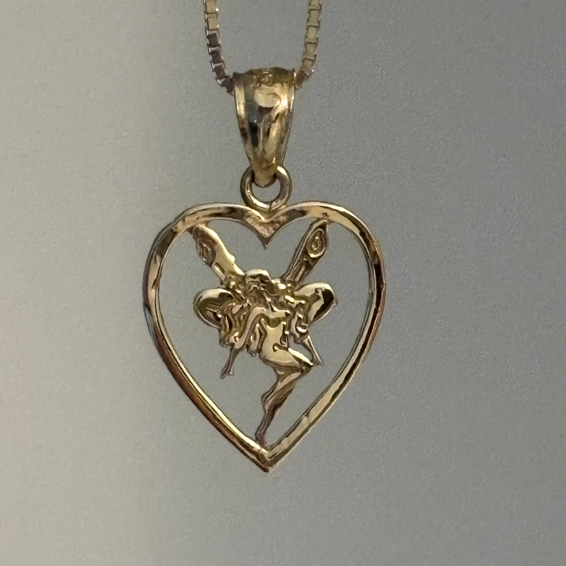 Gold fairy pendant next to a silver coin on a gray background