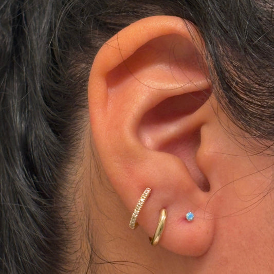 Close-up of an ear with gold hoop earrings and a small blue gemstone earring.