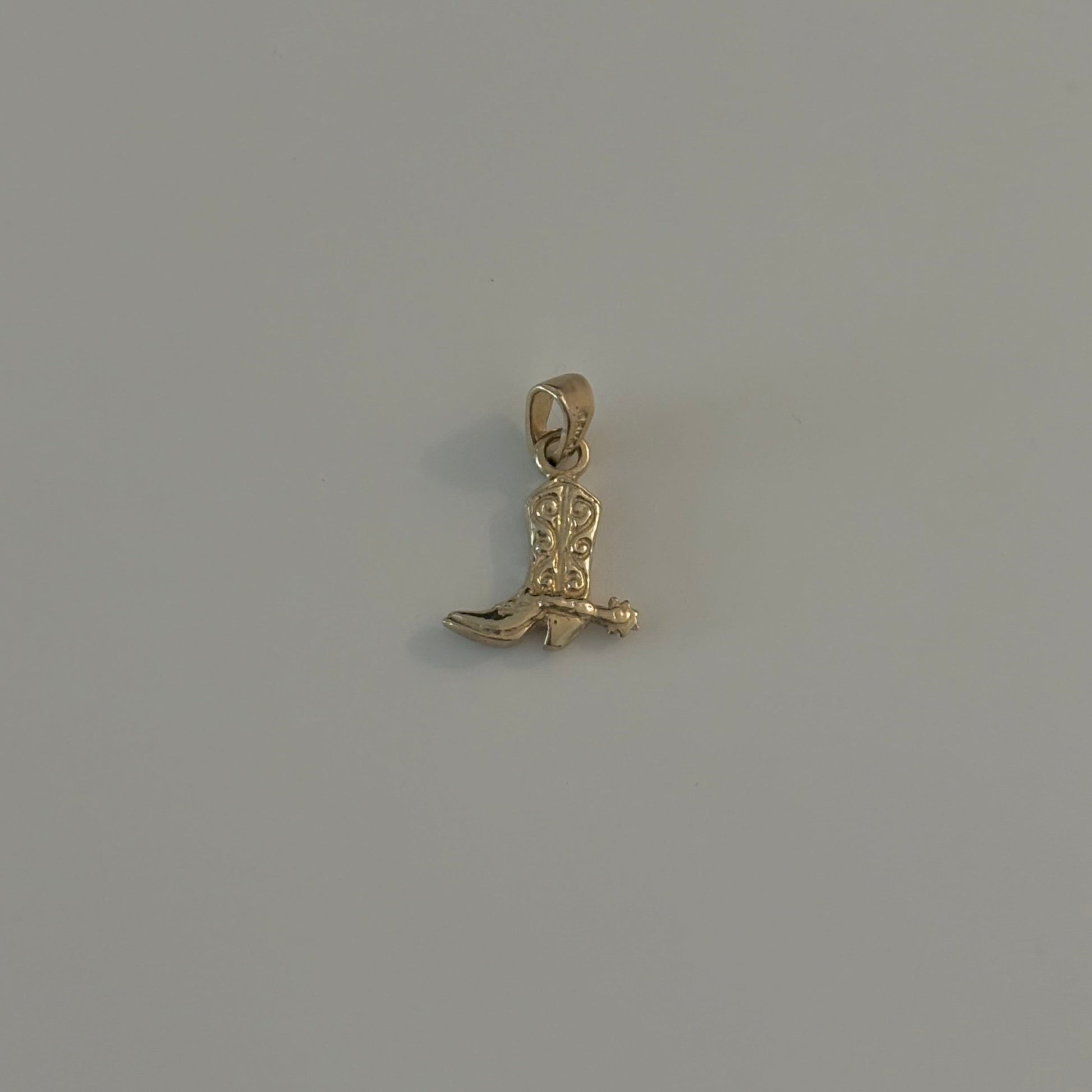 cowboy boot charm Gold pendant on a gray background