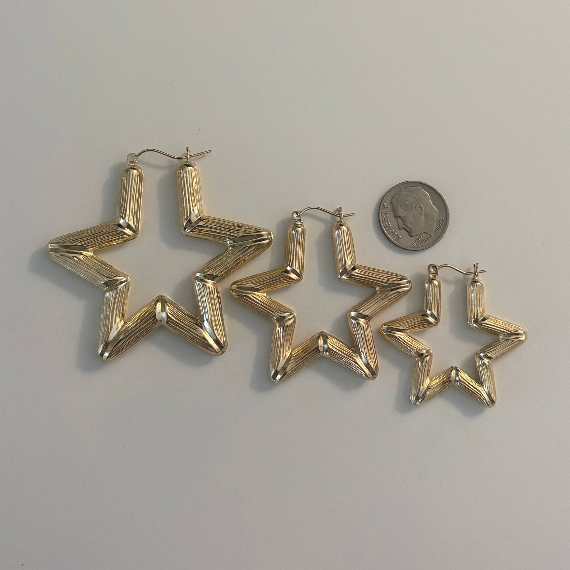 Gold star-shaped earrings next to a coin on a light gray background