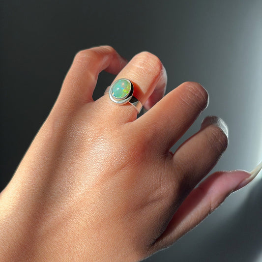 Hand wearing a ring with a green gemstone on a dark background