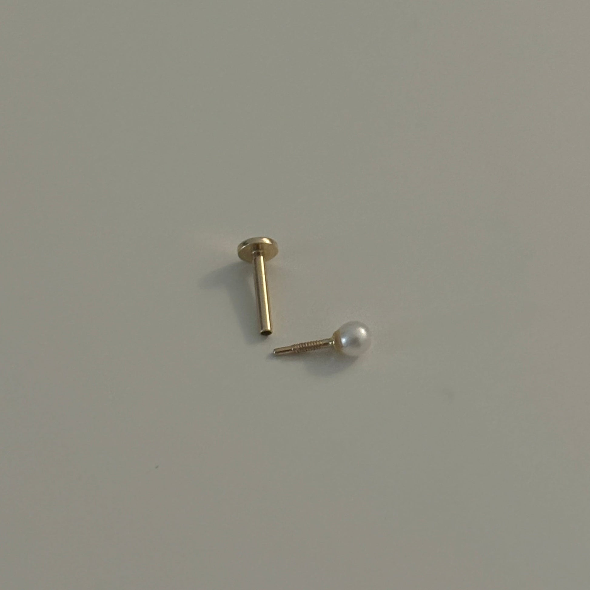 Gold earring with pearl on a light gray background
