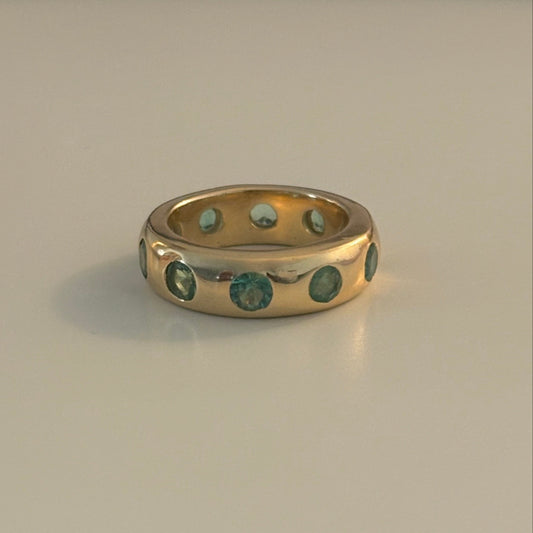 Gold ring with emerald stones on a beige background