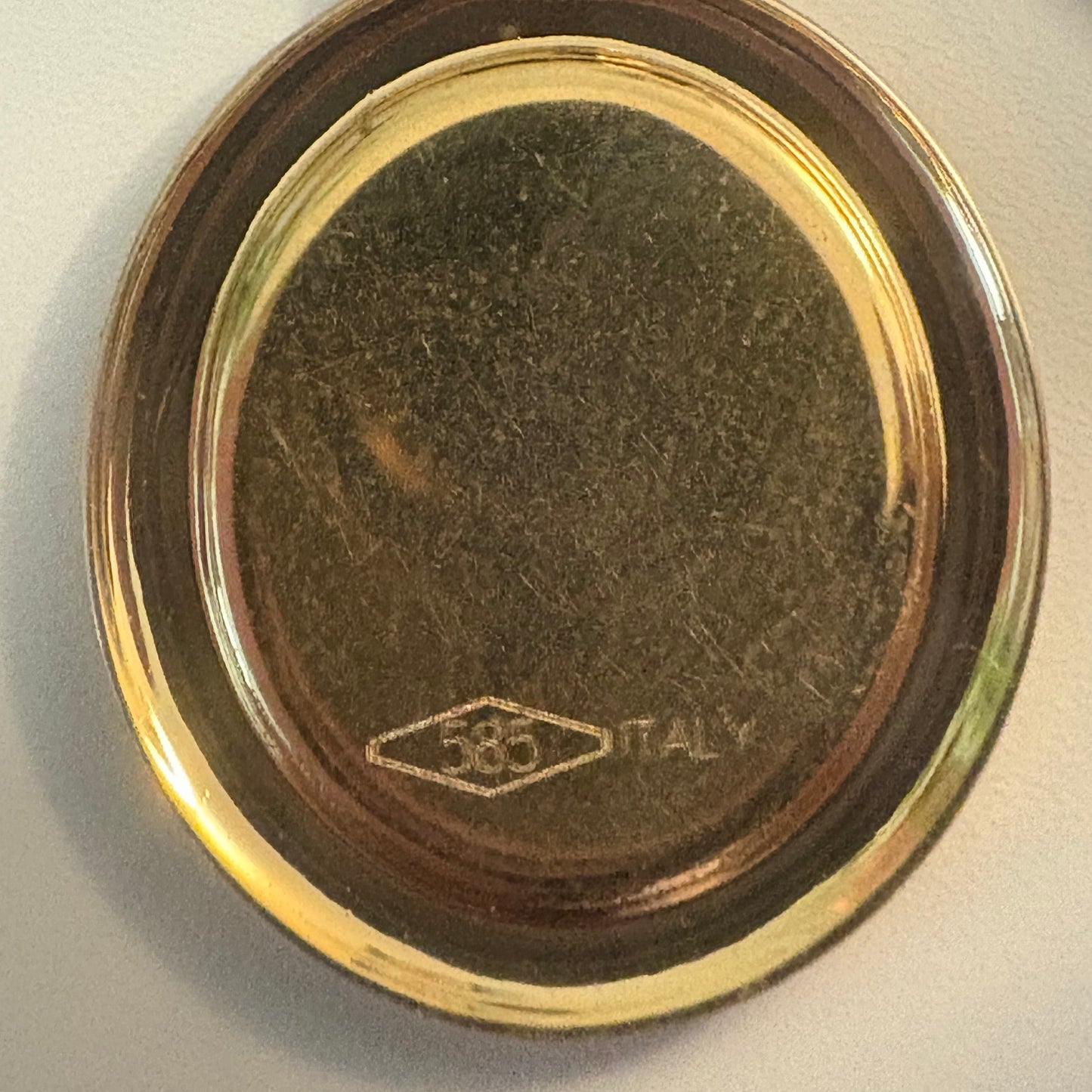 Close-up of a gold and silver object with '585 Italy' engraving on a light gray background