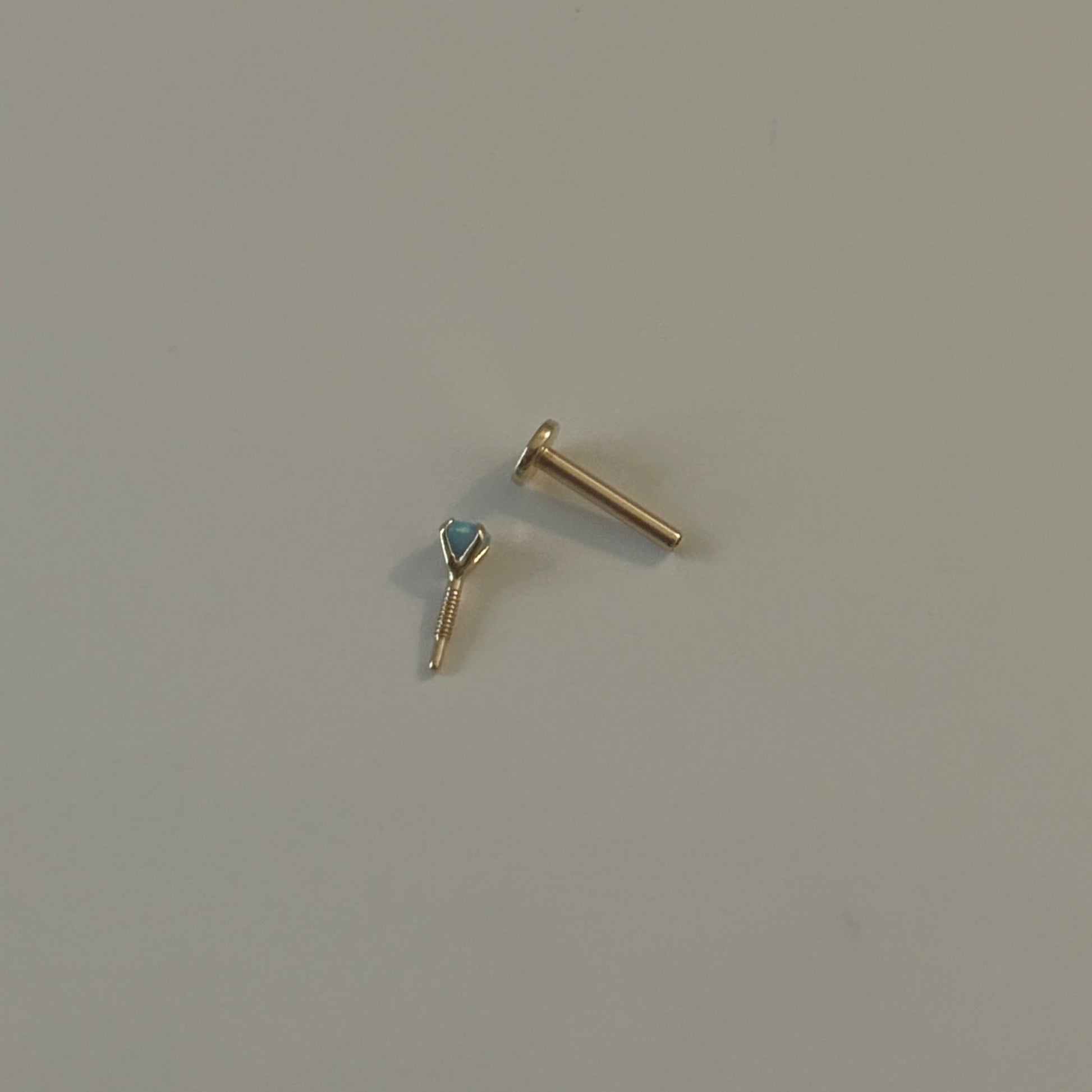 Gold earring with a blue gemstone on a light gray background