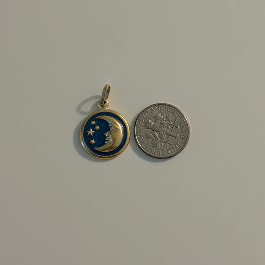 A small round pendant charm with a gold-tone bail, featuring a blue and gold crescent moon and star design, shown next to a silver coin for scale on a plain light gray background.