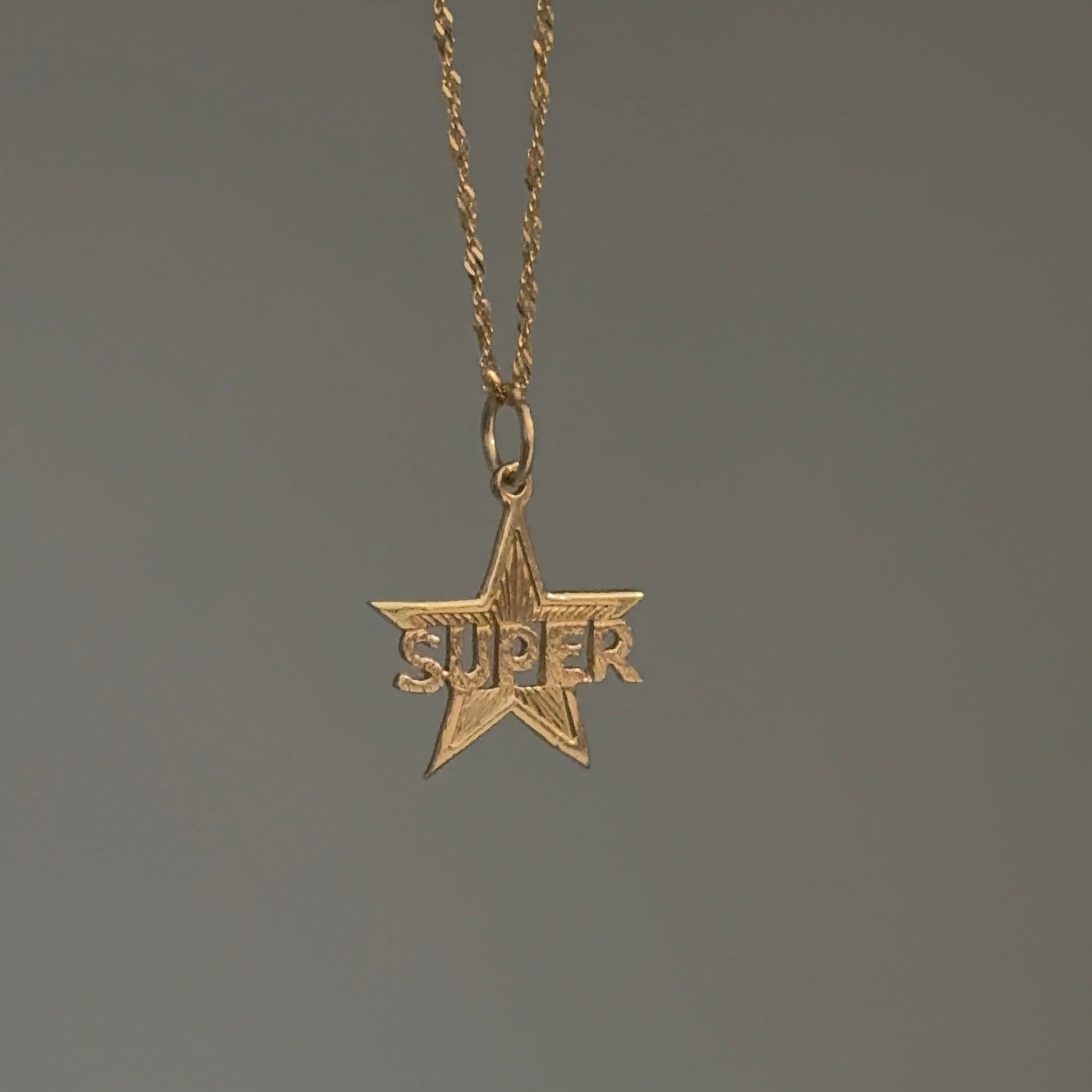 Gold star-shaped pendant with 'SUPER' text on a chain against a dark background