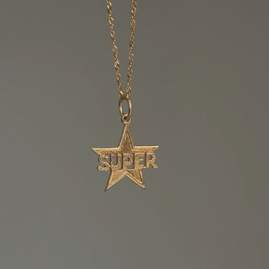 Gold star-shaped pendant with 'SUPER' text on a chain against a dark background
