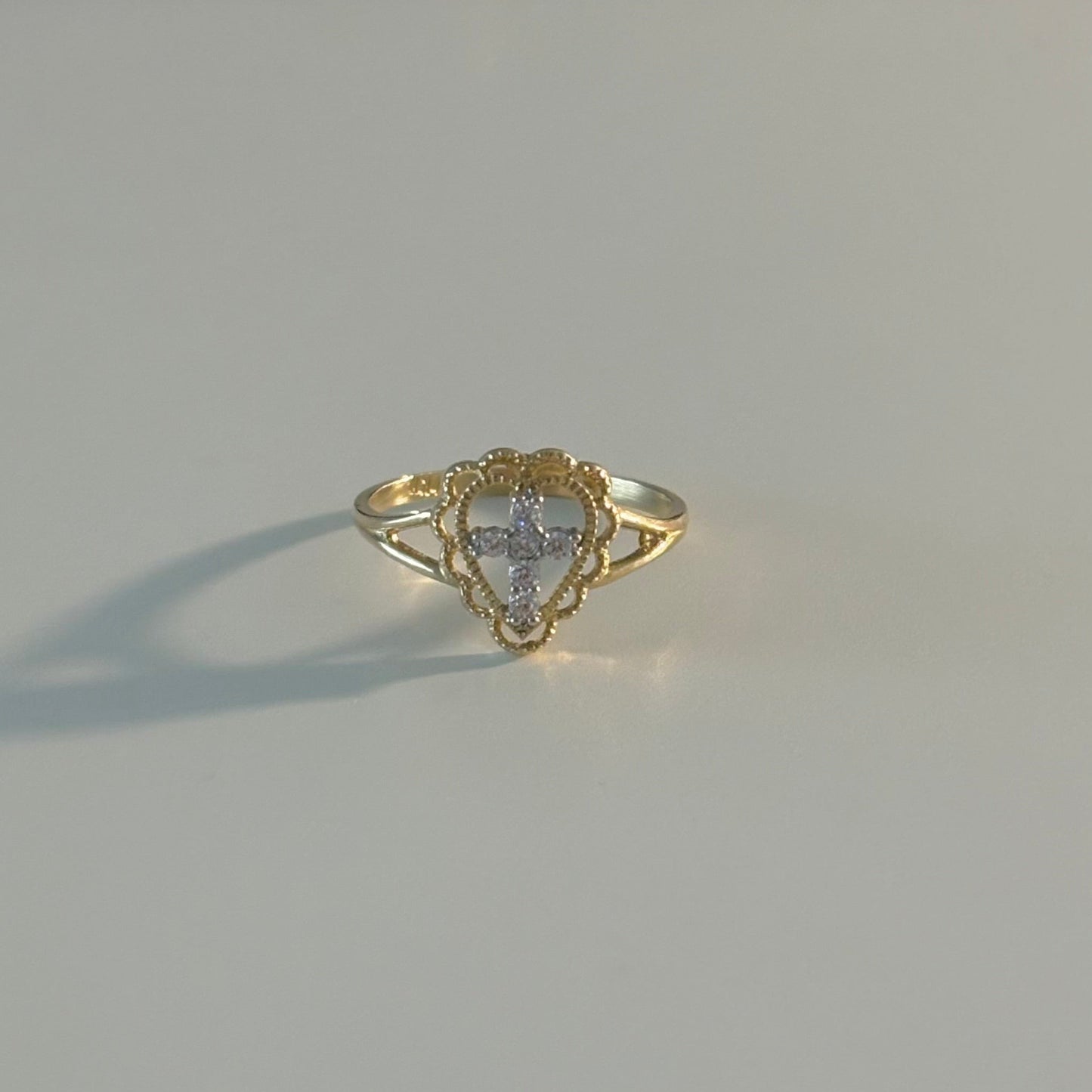 Gold ring with a heart-shaped center on a light gray surface