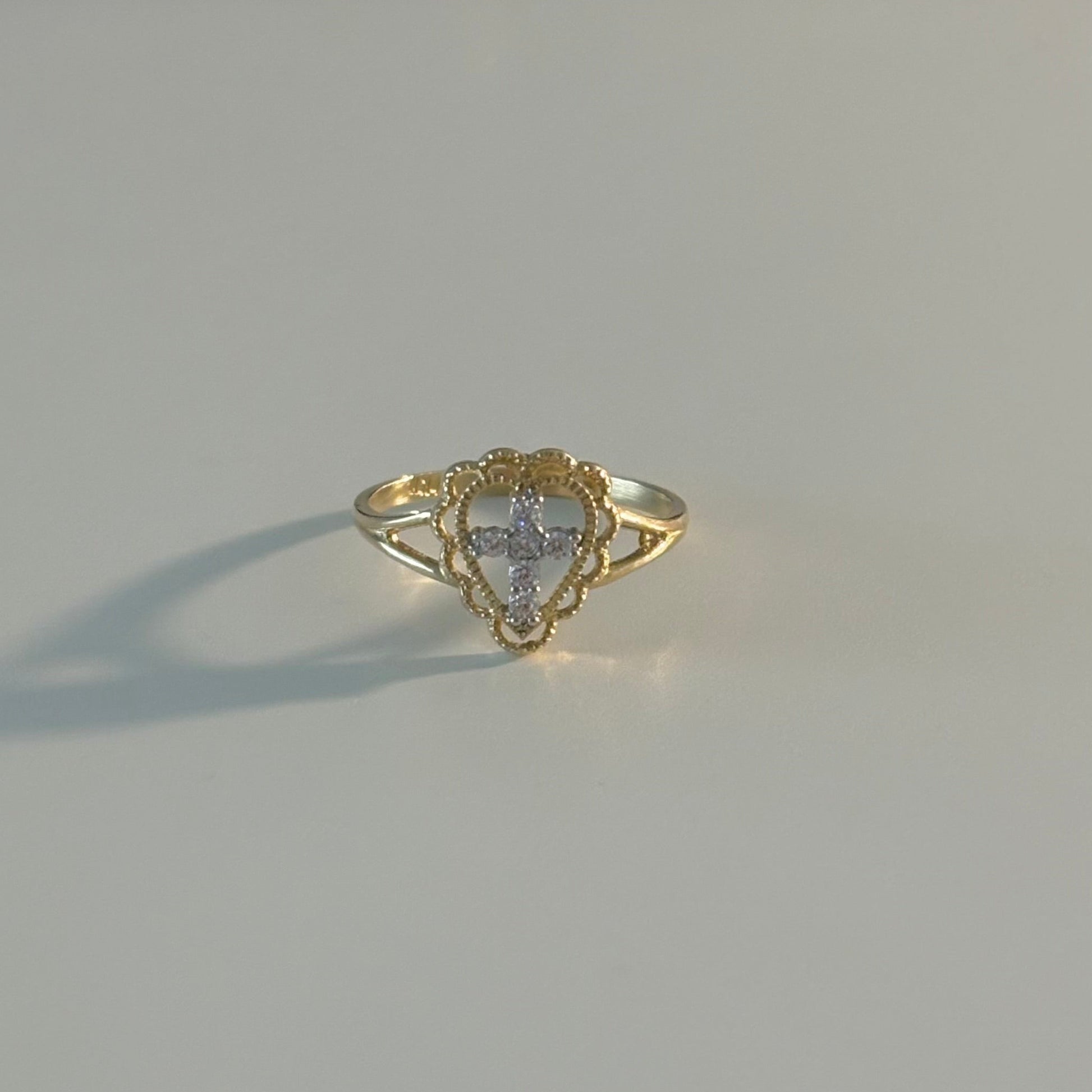 Gold ring with a heart-shaped center on a light gray surface
