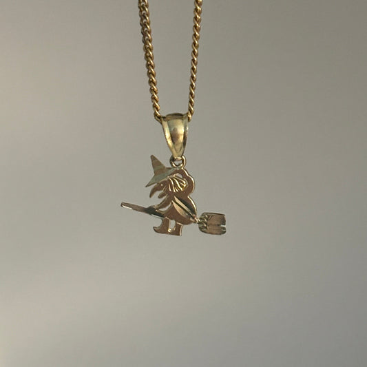 A gold chain necklace with a small witch riding a broomstick pendant, shown against a plain light gray background.