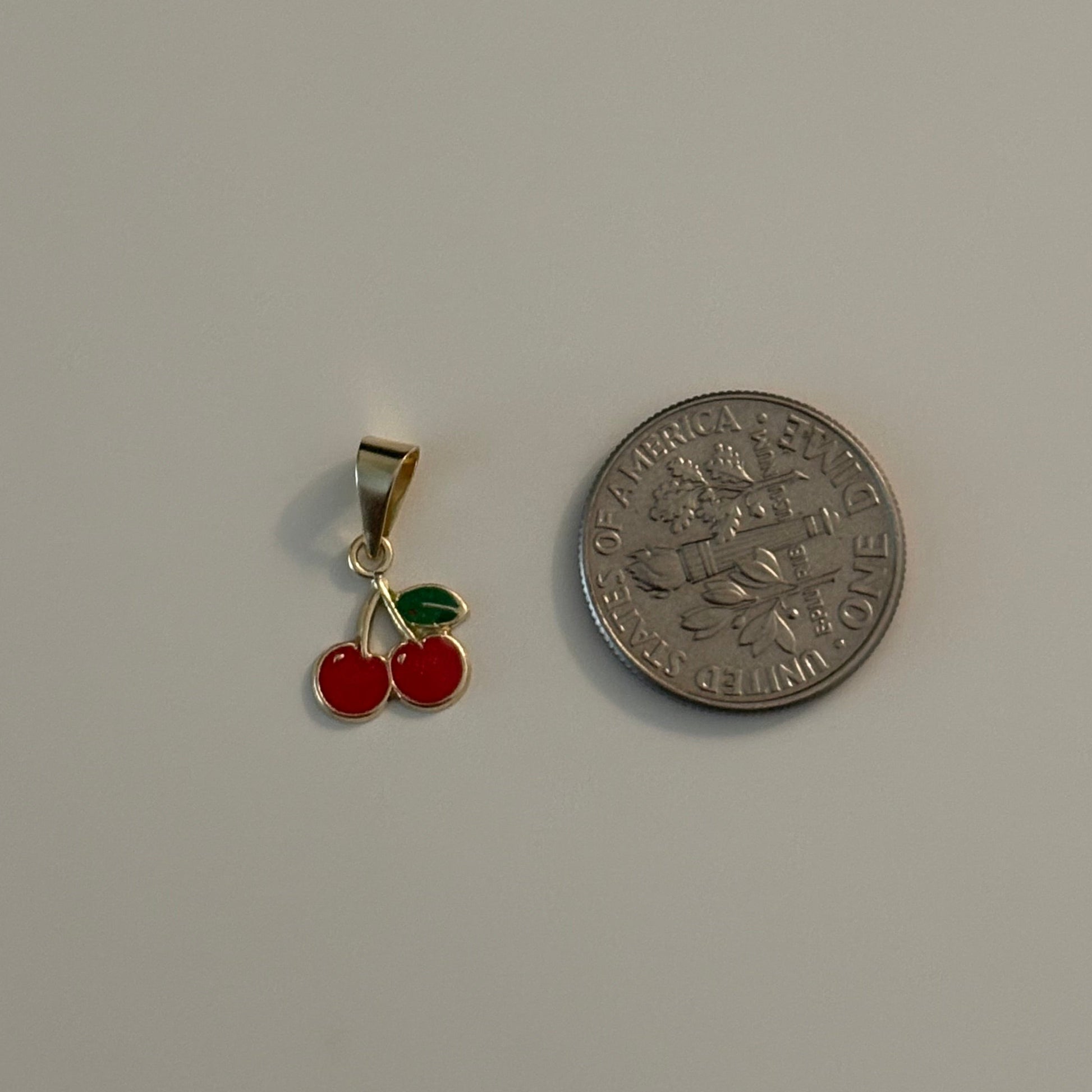 Small gold pendant with red cherries next to a coin on a gray background
