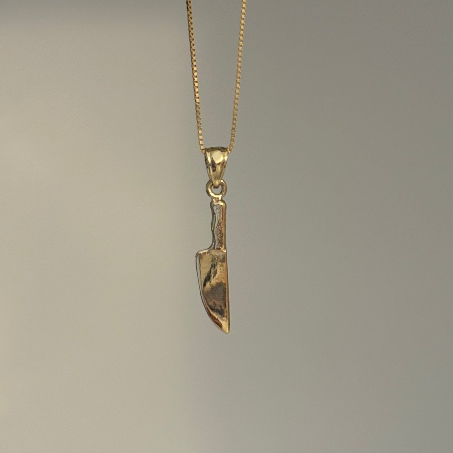 Gold knife-shaped pendant on a chain against a gray background
