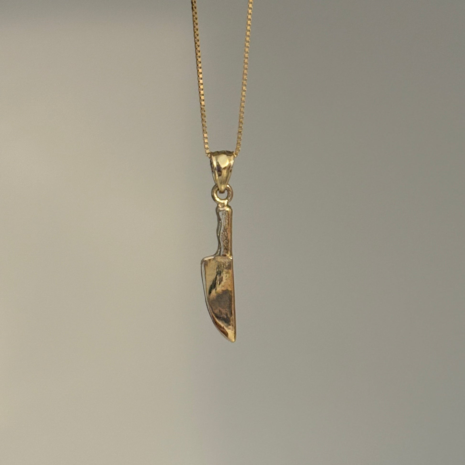 Gold knife-shaped pendant on a chain against a gray background