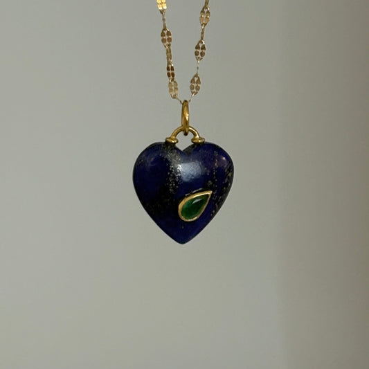 Heart-shaped pendant necklace with blue stone and gold chain on a gray background