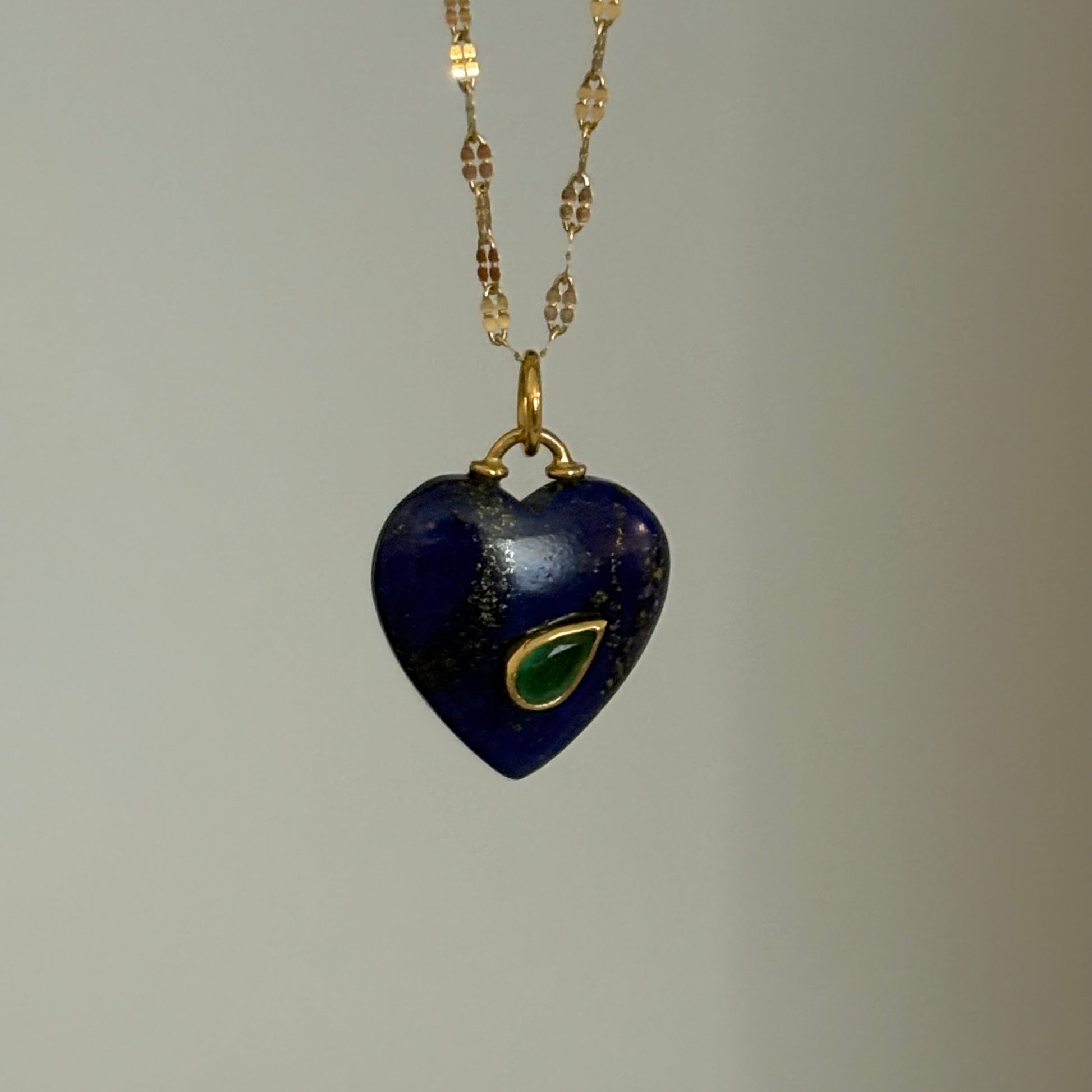 Navy heart-shaped pendant with gold chain on a gray background