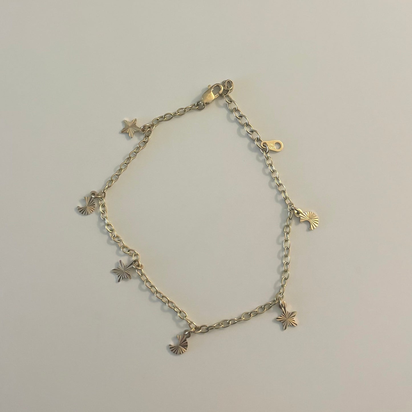 Gold bracelet with star and cross designs on a light gray surface.
